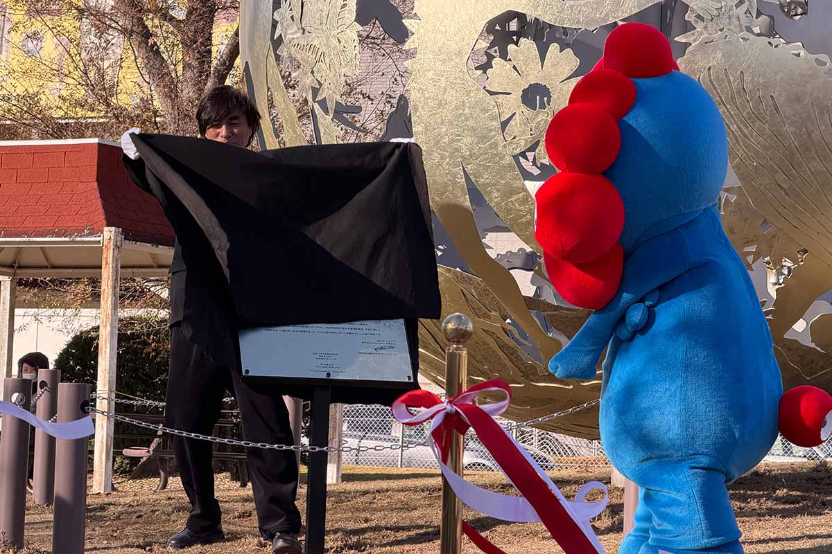 モニュメント「いのち球」移設セレモニーで、除幕した河森正治プロデューサーとミャクミャク（撮影：2025年12月5日）