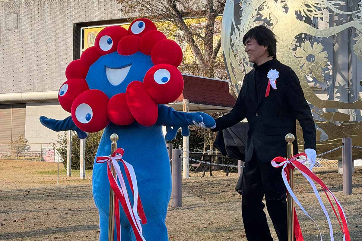 モニュメント「いのち球」移設セレモニーで、除幕した河森正治プロデューサーとミャクミャク（撮影：2025年12月5日）