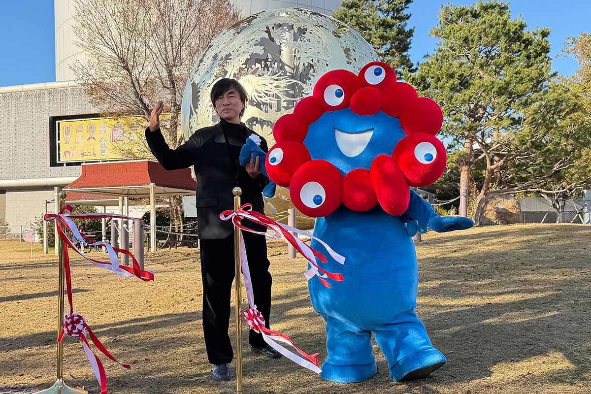 モニュメント「いのち球」移設セレモニーで、除幕した河森正治プロデューサーとミャクミャク（撮影：2025年12月5日）
