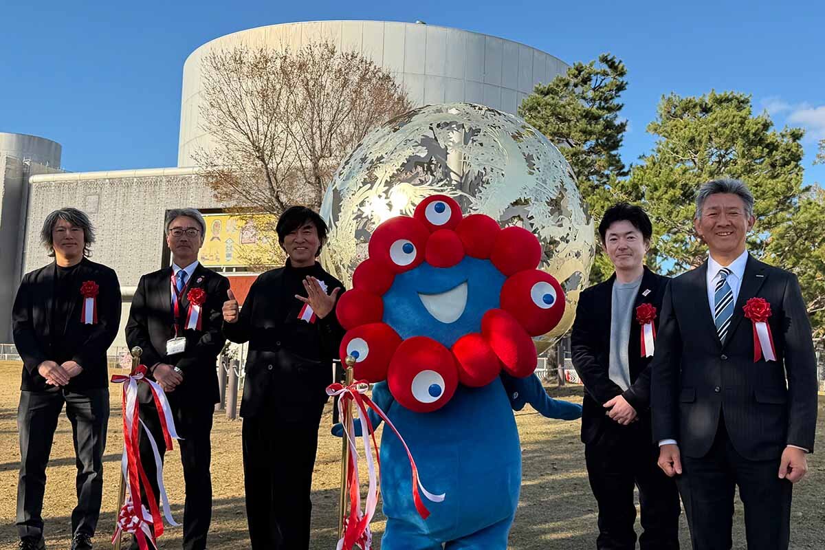 モニュメント「いのち球」移設セレモニーに参加した河森正治プロデューサー（左から3人目）やミャクミャクら関係者（撮影：2025年12月5日）