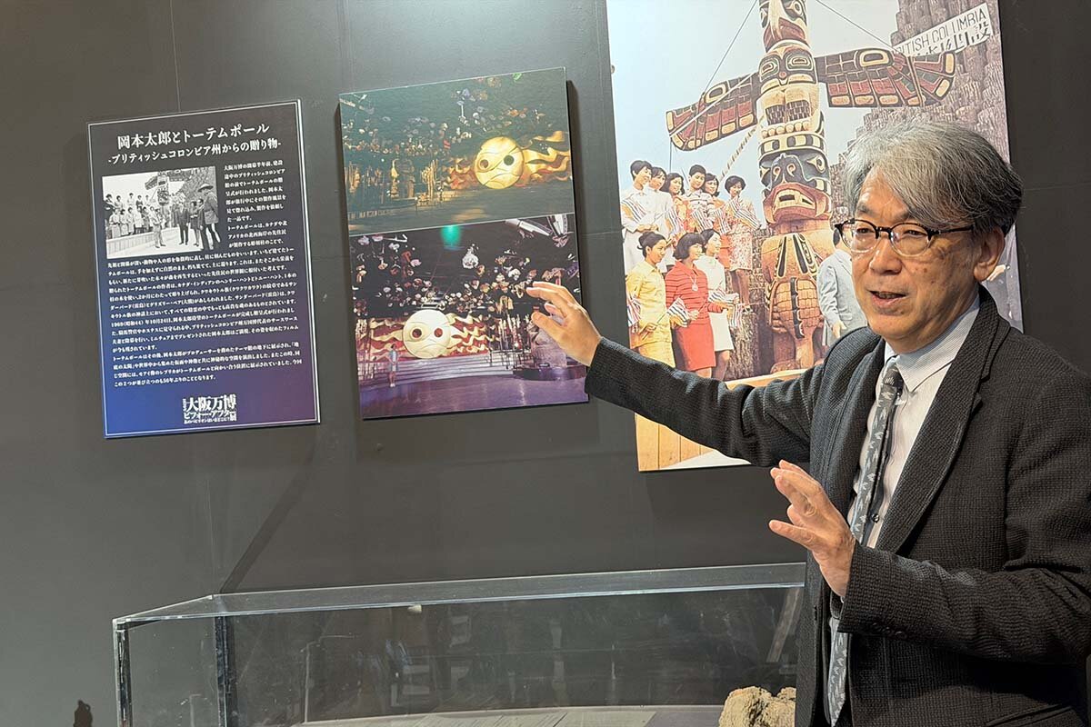 トーテムポールや当時の写真パネルの前で岡本太郎の証言を紹介する橋爪教授（撮影2026年3月16日）