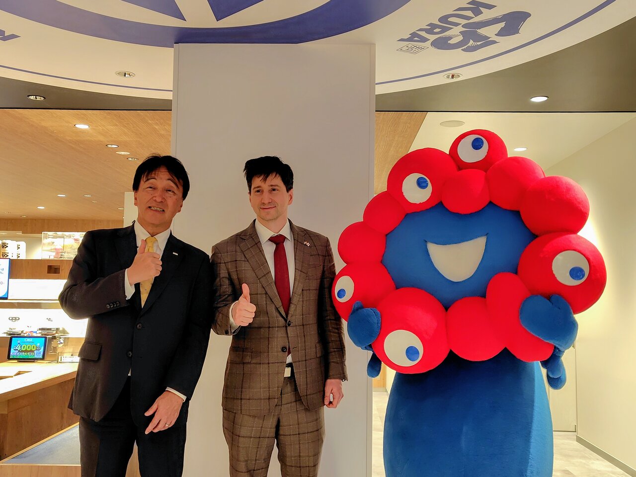 内覧会に駆け付けたミャクミャク（右）。（左から）くら寿司の岡本浩之・取締役、在大阪ハンガリー領事館のケレケシュ・アンドラーシュ領事館長、ミャクミャク（５月13日、大阪市中央区）