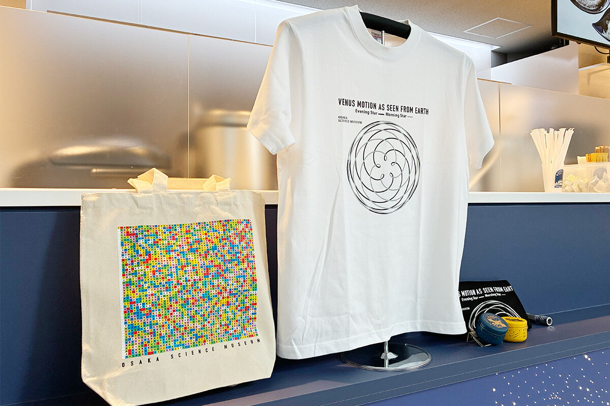 左から「円周率トートバッグ」（2,200円）、星の公転周期の図柄をデザインしたTシャツ（白黒、各2,000円）